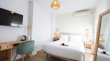Una habitación de hotel moderna con un escritorio de madera, una silla verde, una cama grande con ropa blanca, lámparas de noche y un televisor de pantalla plana montado en la pared.