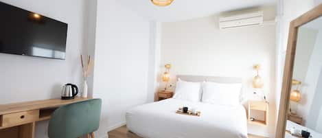 Ett modernt hotellrum med ett skrivbord i trä, en grön stol, en stor säng med vita sängkläder, sänglampor och en platt-TV som är monterad på väggen.