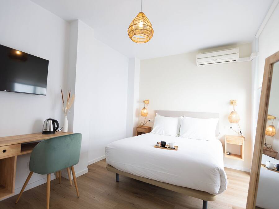 Quarto de hotel moderno com escrivaninha de madeira, cadeira verde, cama grande com roupa de cama branca, abajures e TV de tela plana fixada na parede.
