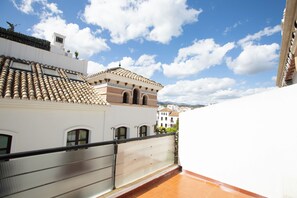 Una terraza en la azotea con techo de baldosas, baranda metálica y vista de edificios circundantes.