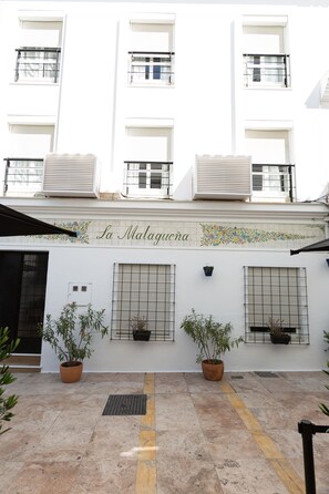 A building facade with the name "La Malaguena" and three potted plants on the ground floor. - Hostal Boutique La Malagueña Only Adults by Croma (Estepona)