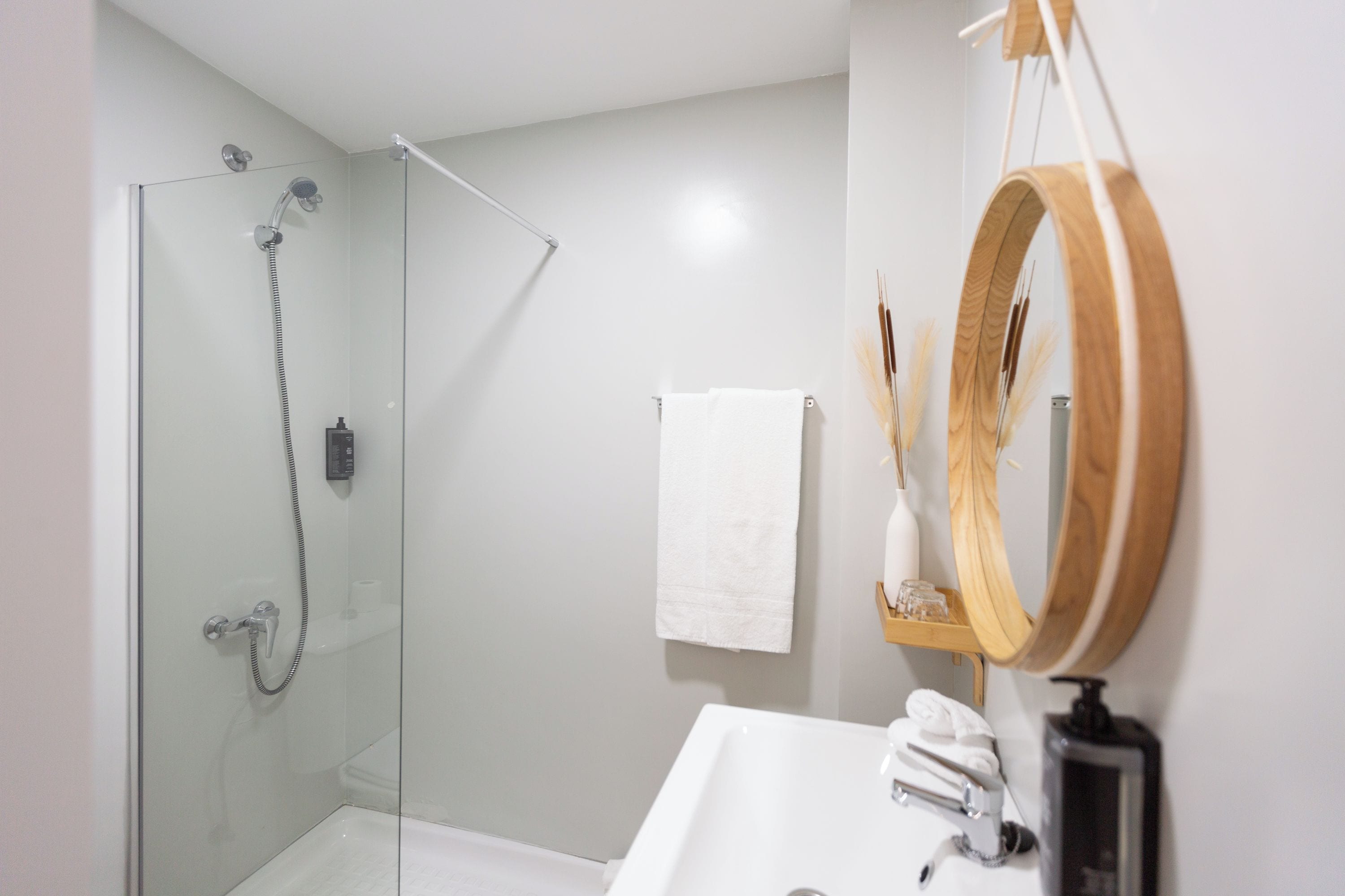 A modern bathroom with a glass-enclosed shower, a white sink, a wooden-framed mirror, and a towel hanging on the wall.