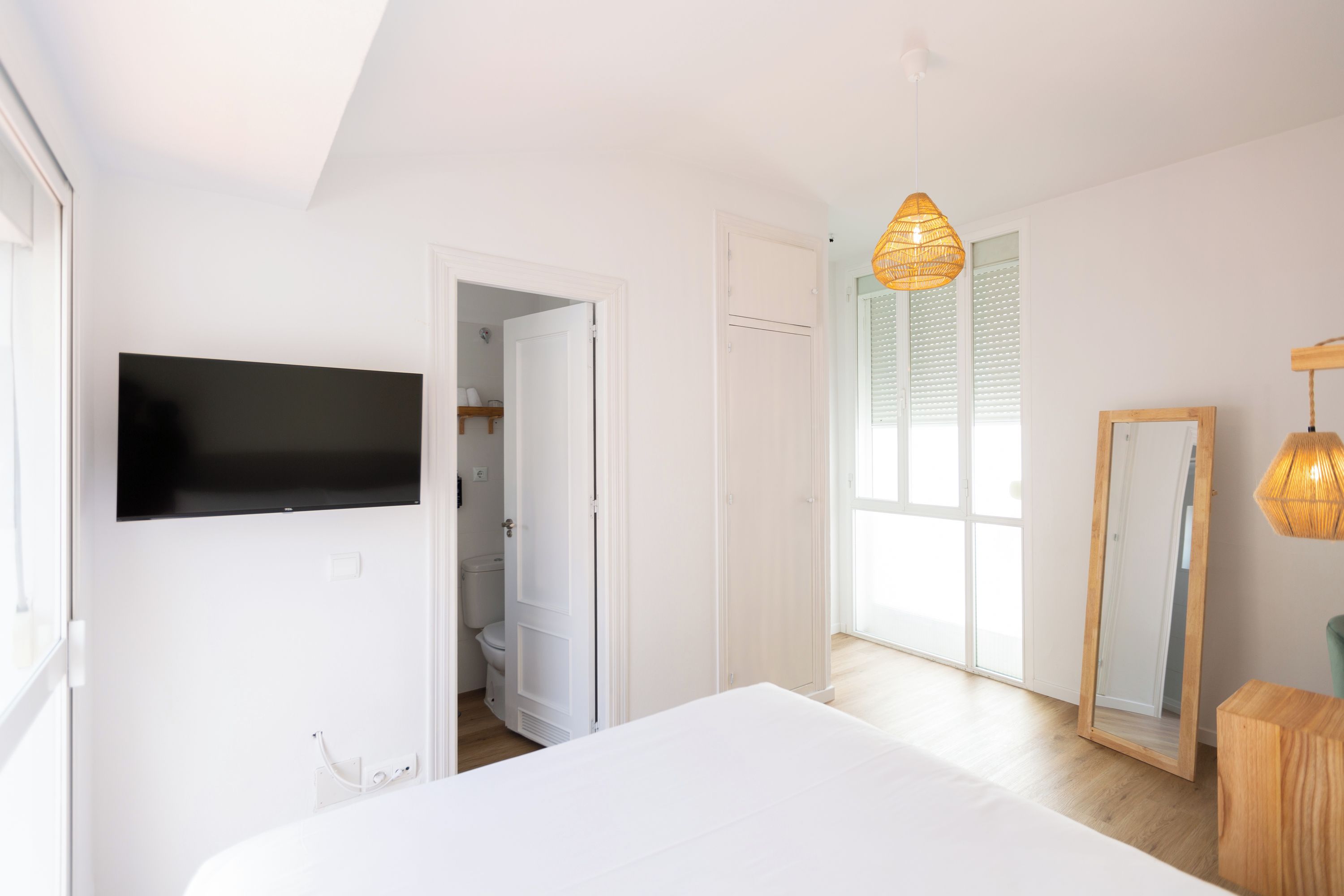 Un dormitorio con cama, televisor montado en la pared, armario y espejo.