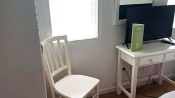Una habitación pequeña con un escritorio blanco, una silla y un monitor de computadora.