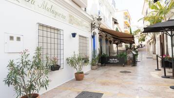 Una calle estrecha con un edificio que dice "La Malagueta". Hay plantas en macetas, mesas al aire libre y un letrero que indica "La Casa del Rey".