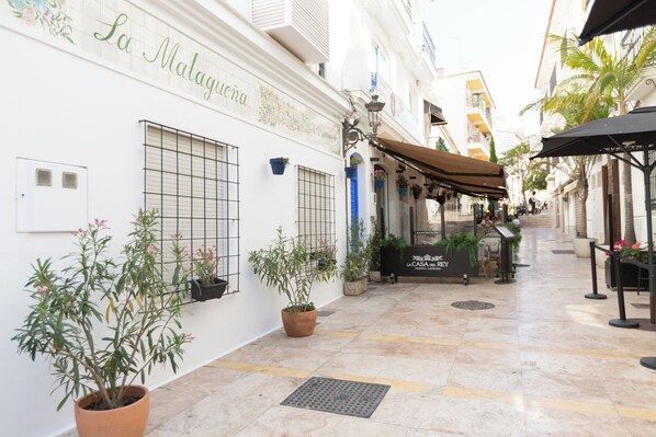 A narrow street with a building labeled "La Malagueta." There are potted plants, outdoor seating, and a sign for "La Casa del Rey." - Hostal Boutique La Malagueña Only Adults by Croma (Estepona)