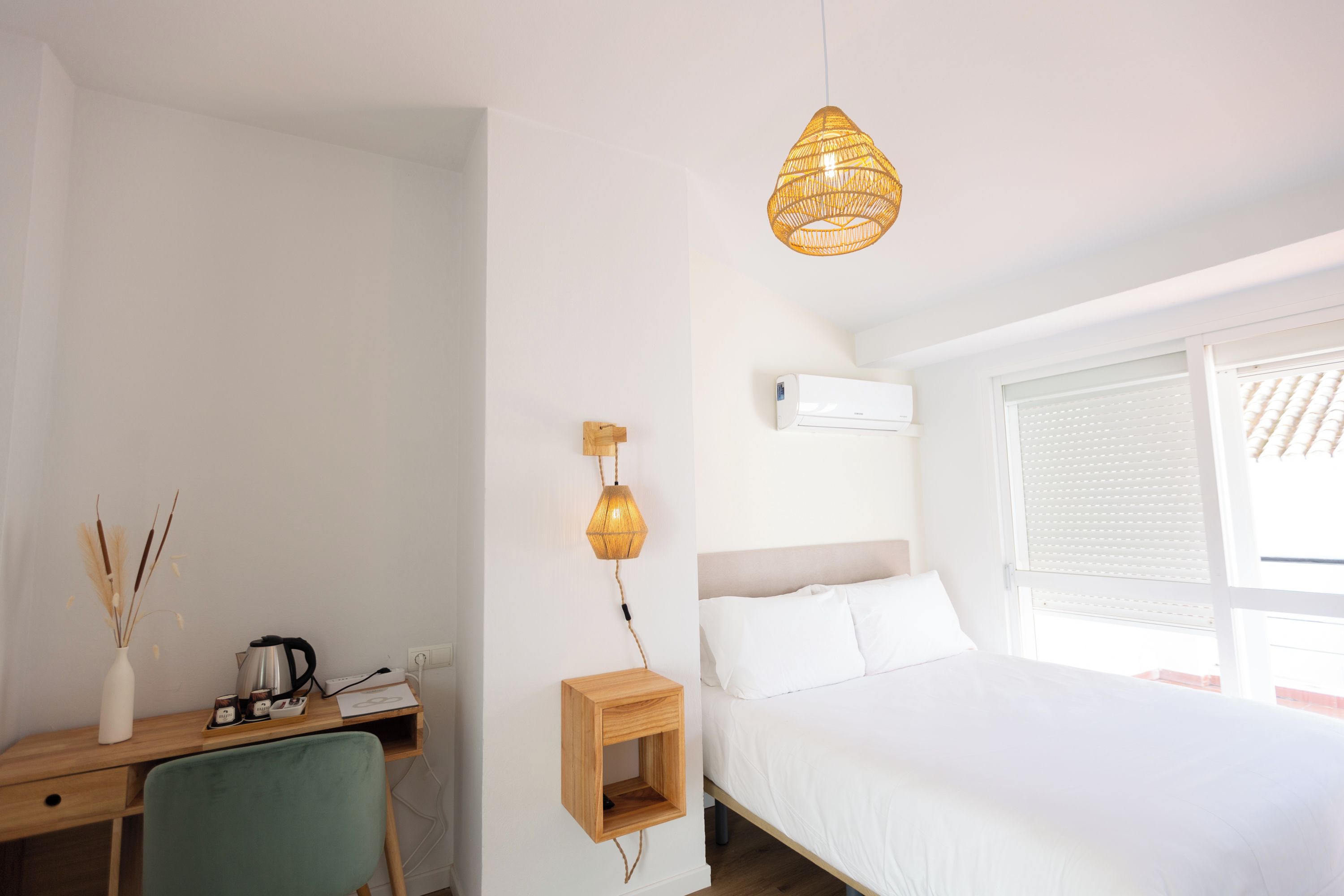 Un dormitorio con una cama, un escritorio con una silla, una lámpara de pared y una ventana con persianas.