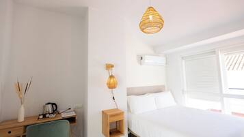 Un dormitorio con una cama, un escritorio con una silla, una lámpara de pared y una ventana con persianas.