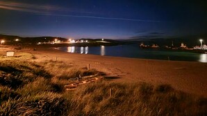 Une scène de plage nocturne, avec une mer calme, des lumières lointaines et un ciel dégagé.