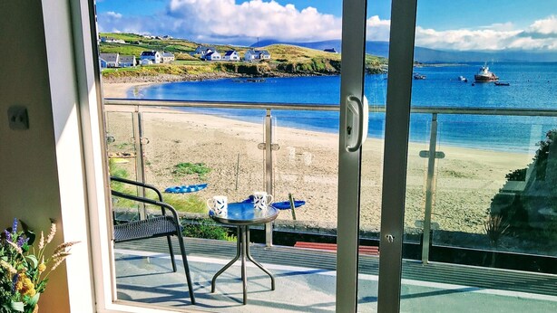 Une pièce dotée d’une grande porte-fenêtre coulissante donnant sur un balcon avec vue sur une plage et l’océan.