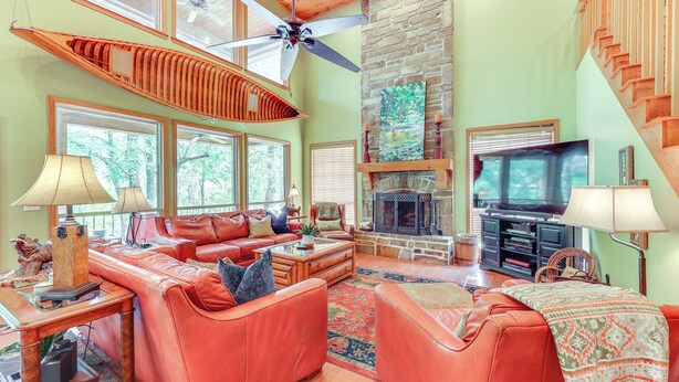 A spacious living room with a large sofa set, a fireplace, a television, and a ceiling fan. - Riverfront Cabin on 2 Acres in Glenwood! (Glenwood)