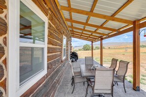 A covered patio with a table and chairs, a grill, and a view of the landscape. - Mountain-View Log Cabin in Wyoming Wilderness (Encampment)