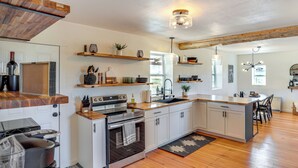 A modern kitchen with white cabinets, a wooden countertop, and a built-in oven. There are shelves above the counter holding various kitchen items and a hanging light fixture.