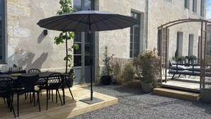 An outdoor patio with a table and chairs, a large umbrella, and potted plants. - Grand Loft Dartiste en Avec Équipement Professionnel Audio et Vidéo (Angoulême)