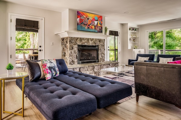 A modern living room with a stone fireplace, a large sectional sofa, and a dark armchair. - Fall Mountain Escape-HeatedPool-HotTub-Sauna-Views (Fairview)