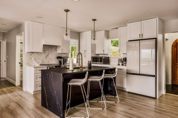 A modern kitchen with white cabinets, a marble backsplash, a central island with bar stools, and stainless steel appliances. - Fall Mountain Escape-HeatedPool-HotTub-Sauna-Views (Fairview)