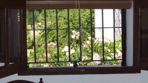 Une fenêtre avec un grillage métallique, un cadre en bois et une vue sur la verdure et des fleurs roses.