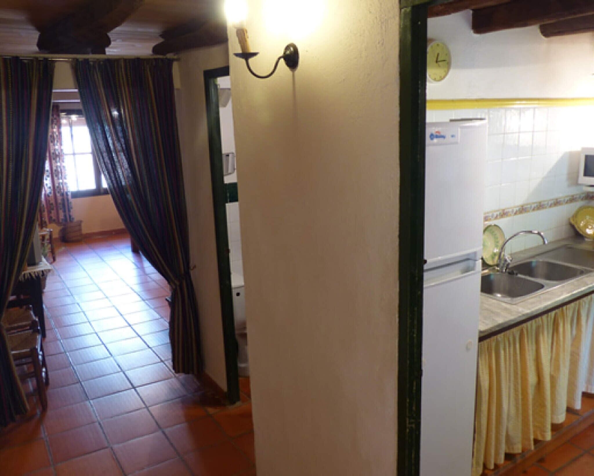 Een gang die uitkomt in een keuken, met een spoelbak en een klok aan de muur.