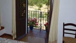 A balcony with a view of a green landscape, a potted plant, and a chair.