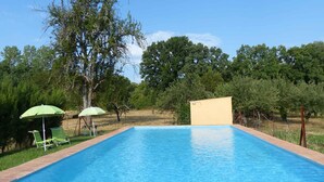 A rectangular swimming pool with a tiled edge, surrounded by a brick border. There are two green umbrellas and two green lawn chairs.