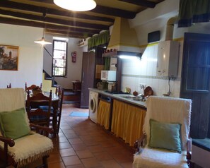 A kitchen with a washing machine, a microwave, and a sink. There are chairs with green cushions and a staircase leading to another room. - Country House 'Los Cascos' with Mountain View, Shared Pool and Air Conditioning (Huelva)