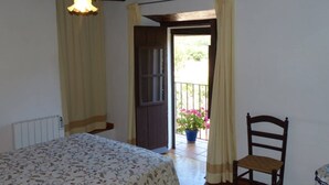 A bedroom with a bed, a chair, a balcony with a potted plant, and a door leading outside.