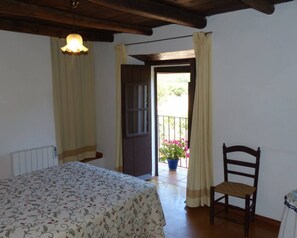 Une chambre à coucher avec un lit, une chaise, un balcon agrémenté d’un pot de fleurs et une porte donnant sur l’extérieur.
