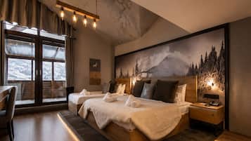 A modern bedroom with a large bed, a desk, and a view of mountains through large windows.