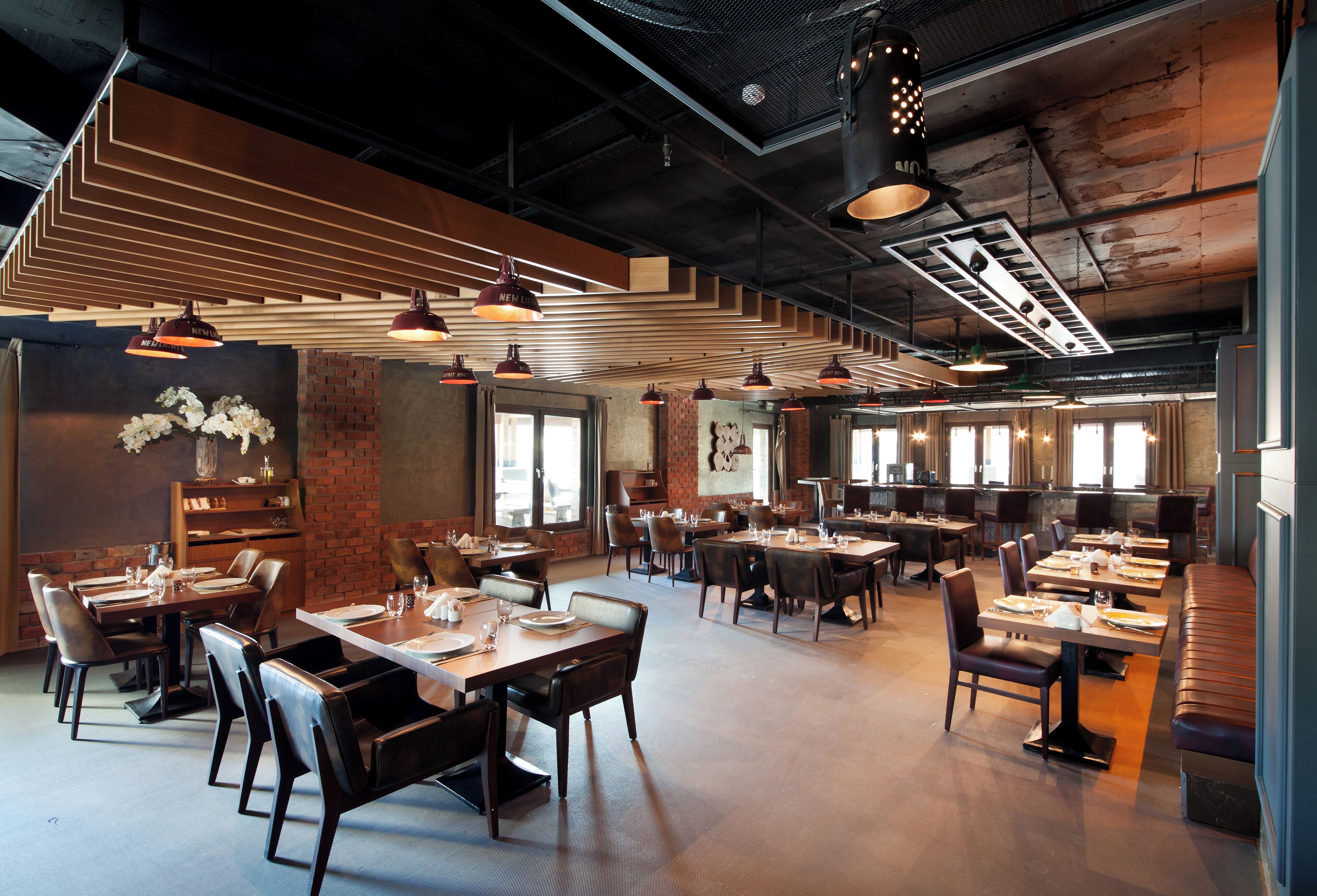 A spacious restaurant with multiple dining areas, wooden tables, and modern pendant lighting.
