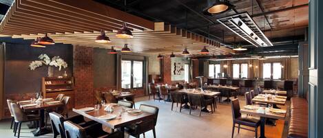 A spacious restaurant with multiple dining areas, wooden tables, and modern pendant lighting.