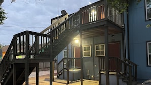 Un edificio de dos pisos con escalera de madera, balcón y puerta con ventana.