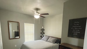 Un dormitorio con cama, ventilador de techo, cómoda, espejo y una cita motivacional en la pared.