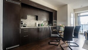 Een moderne keuken met donkere kastjes, een eethoek met zwarte stoelen en een stadszicht door grote ramen.