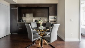 Een moderne keuken met donkere kastjes, een ronde glazen tafel en twee grijze stoelen.