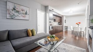 A modern living room with a grey sofa, a glass coffee table, and a painting on the wall.
