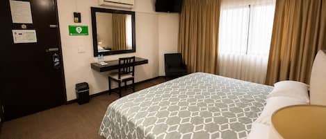 A hotel room with a bed, desk, chair, and a ceiling fan.