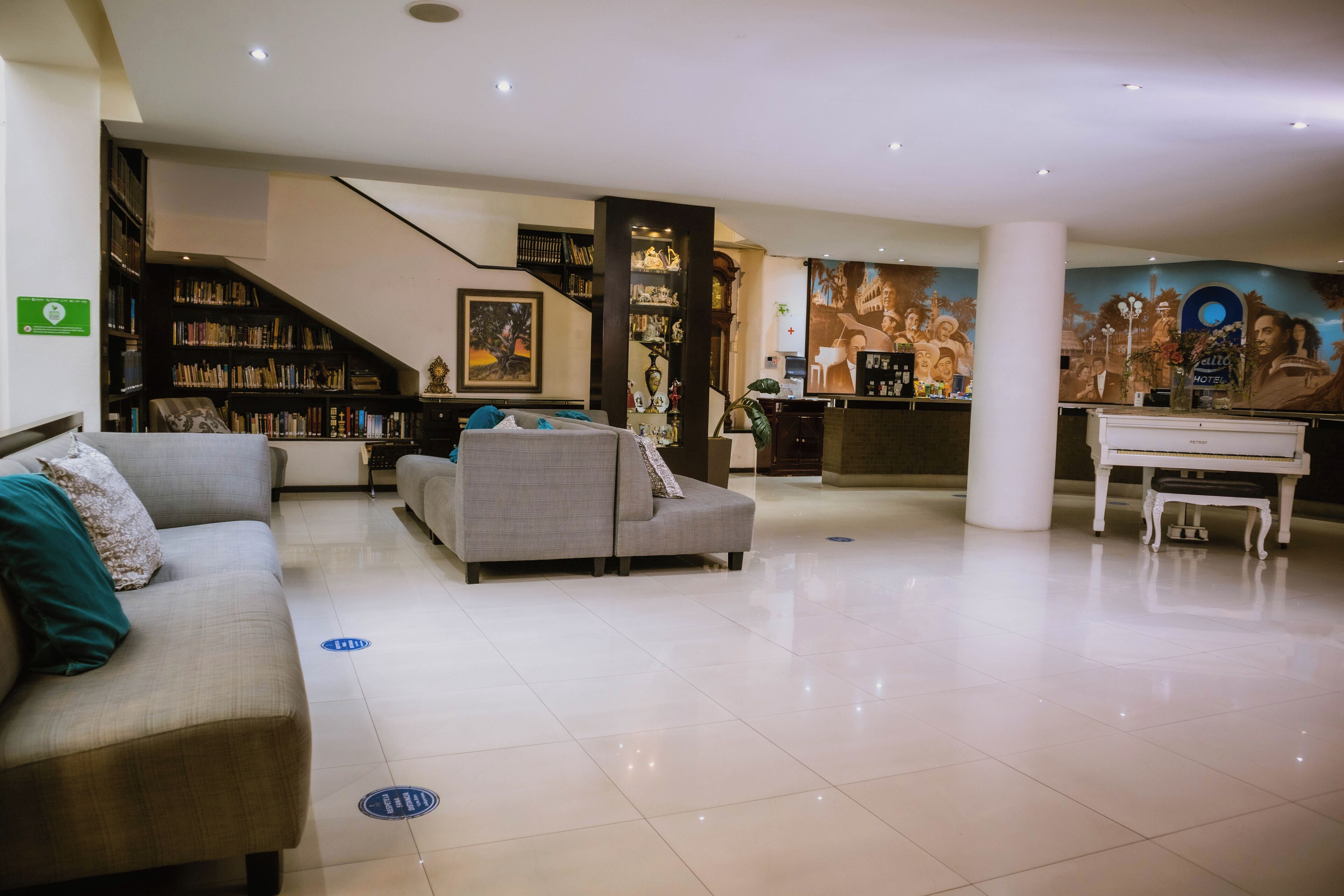 A spacious hotel lobby with a modern design, featuring a large sofa, a piano, and a bookshelf.