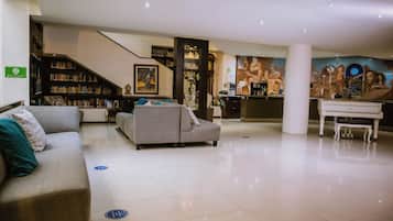 A spacious hotel lobby with a modern design, featuring a large sofa, a piano, and a bookshelf.