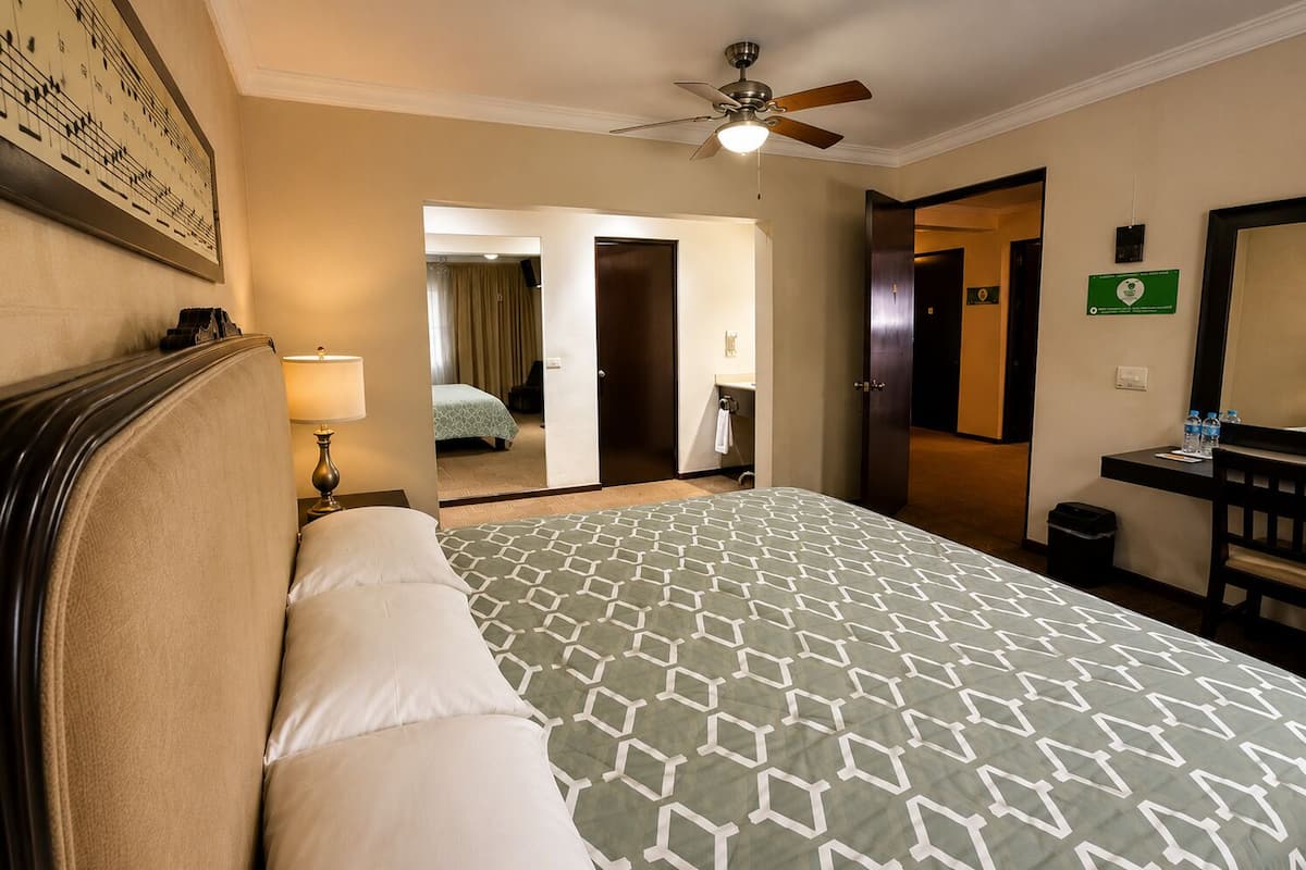 A hotel room with a bed, a desk, a chair, a ceiling fan, and a bathroom visible through an open door.