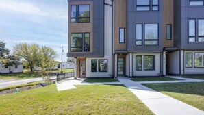Un edificio residencial moderno de varios pisos, con techo plano, ventanas amplias y un césped bien cuidado.