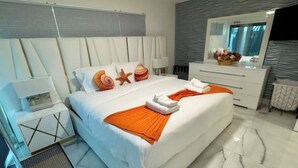 A modern hotel room with a large bed, white bedding, an orange throw, a starfish decoration, and a large mirror above the dresser. - Amazing Home w/ Heated Pool 8 mins to the Beach! (Lighthouse Point)