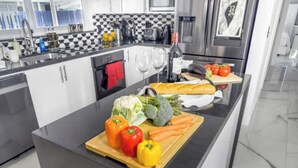 A modern kitchen with a black countertop, a cutting board with vegetables, and a stainless steel sink. - Amazing Home w/ Heated Pool 8 mins to the Beach! (Lighthouse Point)