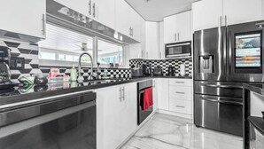 A modern kitchen with stainless steel appliances, a black and white checkered backsplash, and a large window providing natural light. - Amazing Home w/ Heated Pool 8 mins to the Beach! (Lighthouse Point)
