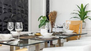 A modern dining area with a glass table, white chairs, and a decorative plant. - Amazing Home w/ Heated Pool 8 mins to the Beach! (Lighthouse Point)