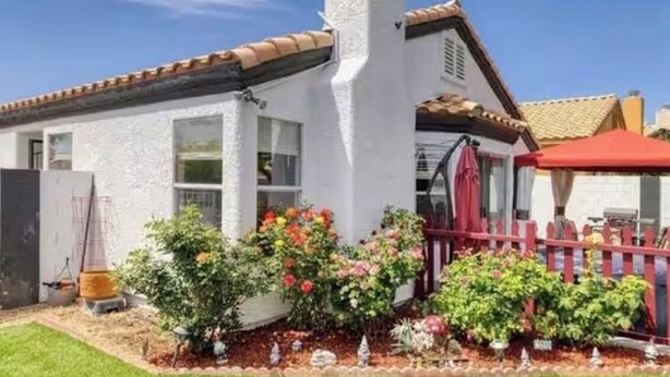 A white house with a red roof, a chimney, and a fenced garden with flowers. - Bright, pet-friendly home near Summerlin and The Lakes (Las Vegas)