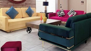 A living room with a yellow sofa, a pink sofa, a green sofa, and a red chair. There is a ceiling fan, a round mirror, and a lamp. - Bright, pet-friendly home near Summerlin and The Lakes (Las Vegas)