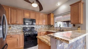 A kitchen with wooden cabinets, a granite countertop, a stove, and a ceiling fan. - Bright, pet-friendly home near Summerlin and The Lakes (Las Vegas)