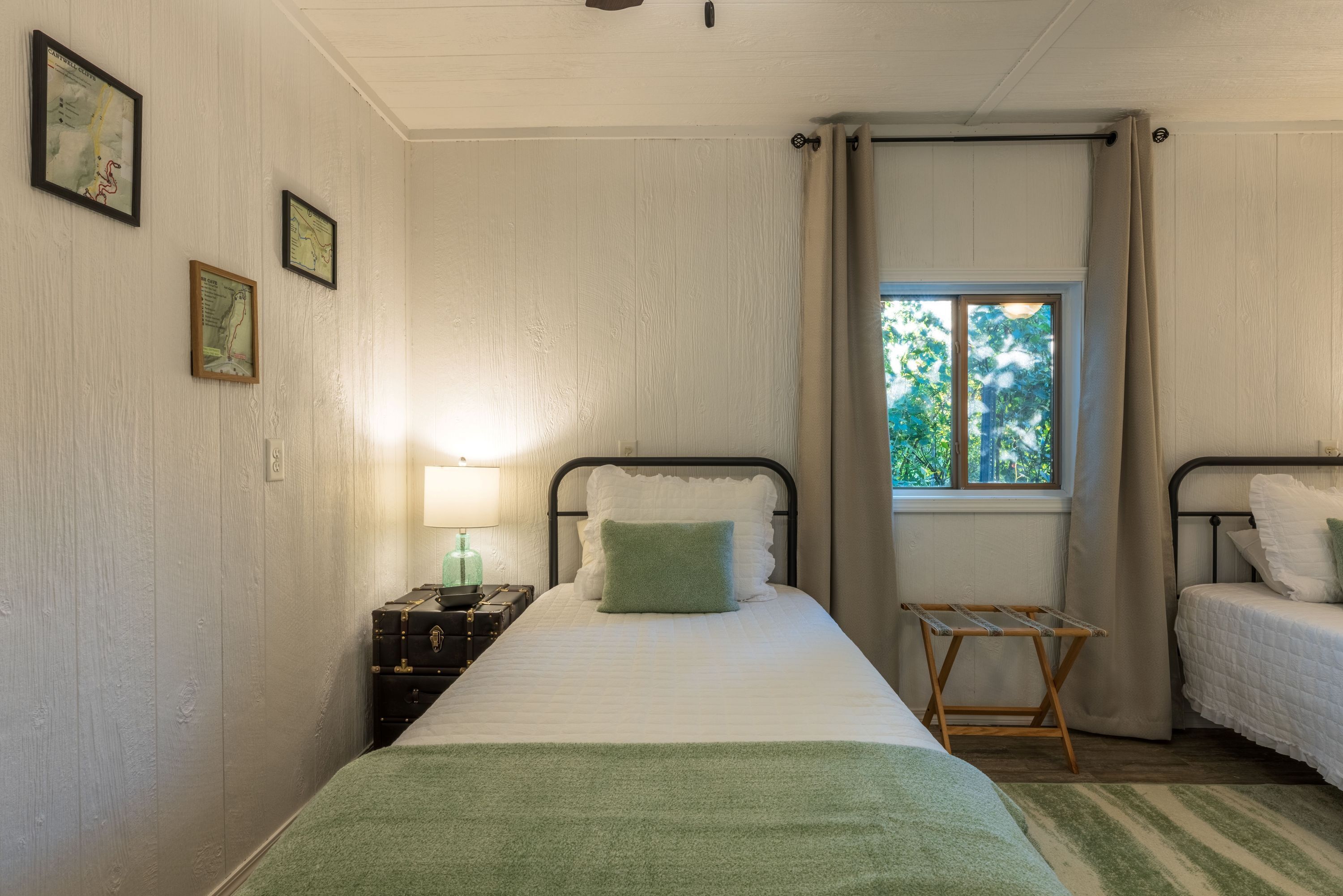Een kamer met een bed, een nachtkastje met lamp, een raam met gordijnen en een kleine tafel met een droogrek.