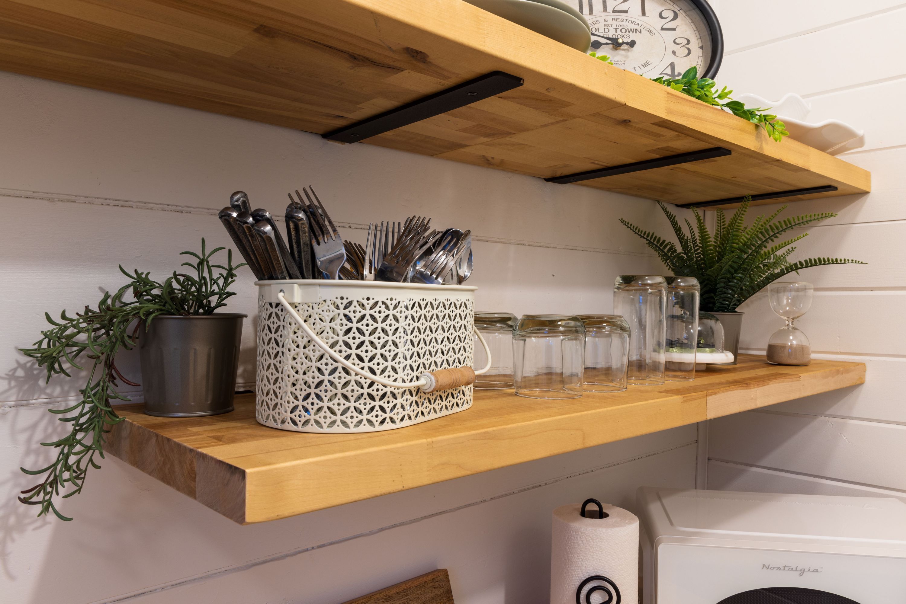 Une étagère de cuisine avec des ustensiles, des bocaux et une horloge.