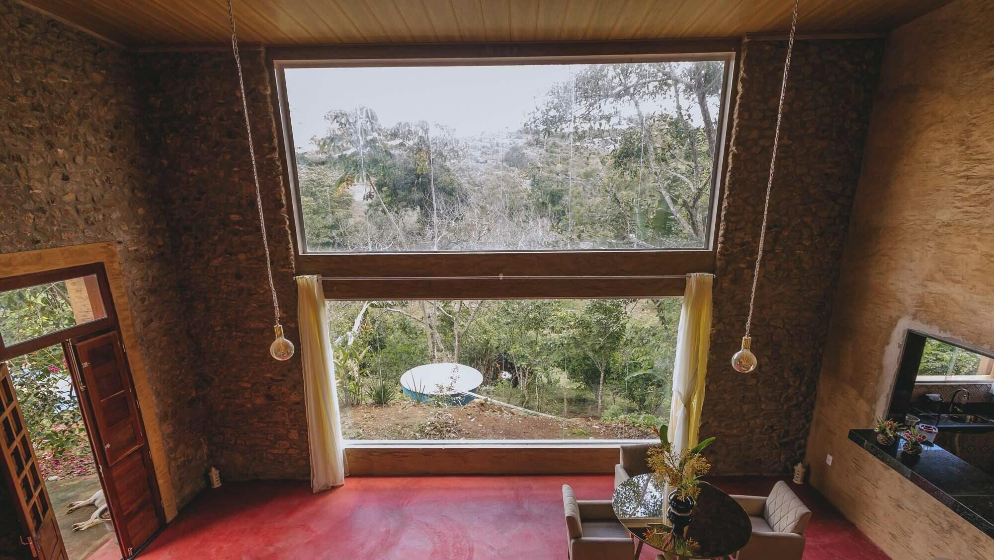 A room with a large window, a red floor, and a view of trees and a white structure outside.